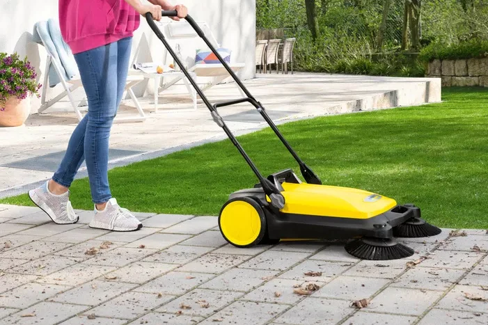 Person kehrt Terrasse mit Kehrmaschine